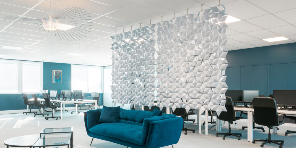 Progetto di uffici open space con divisorio sospeso Facet in azzurro che crea privacy tra area lounge e postazioni di lavoro a Mérignac