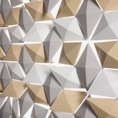 Nahaufnahme des Facet-Raumteilers in Beige, Perlgrau und Weiß mit abgewinkelten geometrischen Elementen, die Tiefe und Schatten erzeugen.